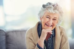 Smiling elderly lady wearing a tan cardigan with her chin resting on her hand