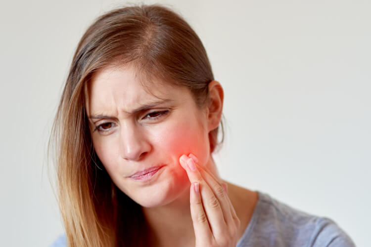 Girl with fingers on her cheek and a red glow indicating tooth pain which can be remedied by root canal therapy