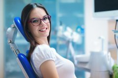 Young adult brunette woman with glasses smiling as she awaits treatment in the dental chair