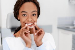 Pretty smiling black girl holding a clear aligner