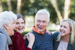 White haired grandparents smiling & laughing with two young adult granddaughters.